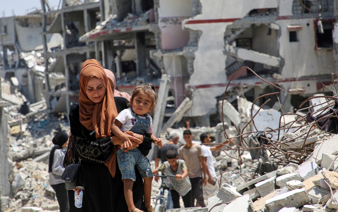 A Palestinian woman holds her daughter as she walks past the rubble of houses destroyed during the Israeli military offensive, amid Israel-Hamas conflict, in Khan Younis in the southern Gaza Strip July 10, 2024. REUTERS