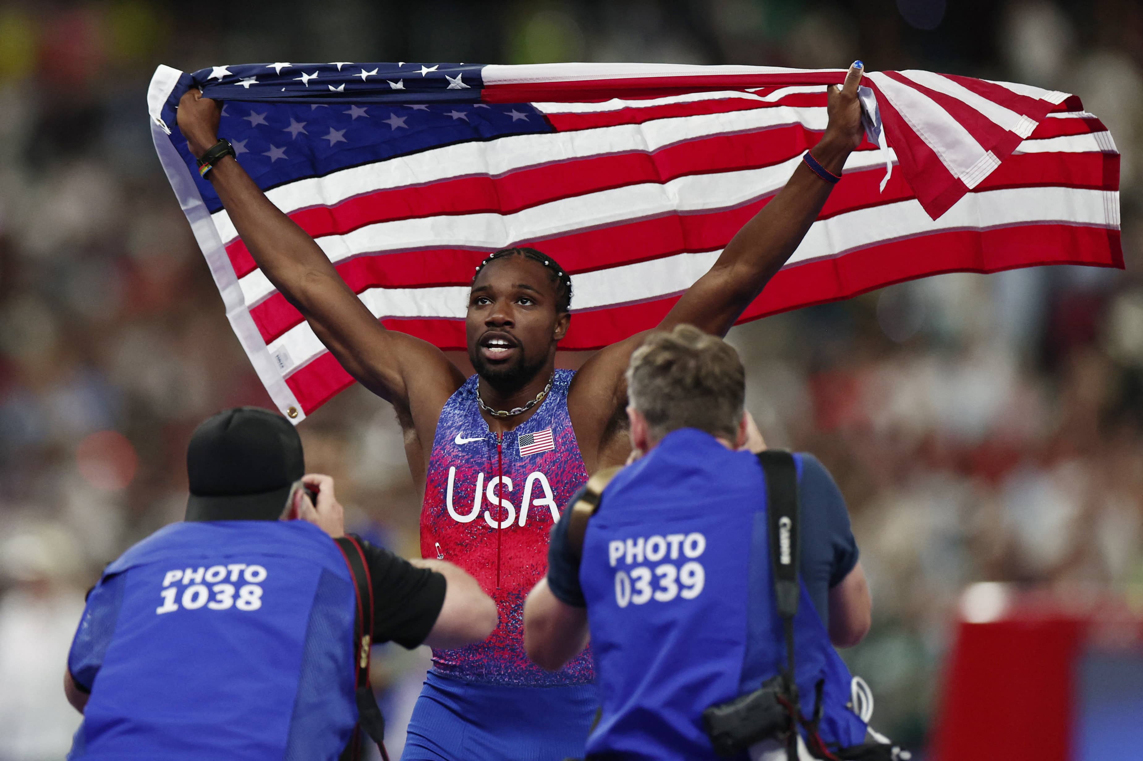 PARIS 2024: Lyles wins 100 metres gold by a whisker - Noah Lyles of United States celebrates with his national flag after winning gold. REUTERS/Kai Pfaffenbach