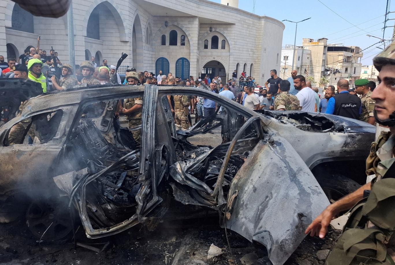 People and Lebanese army members stand near a burnt car after an Israeli strike on the outskirts of the southern port city of Sidon, according to two Palestinian sources, in Lebanon August 21, 2024. (Photo: REUTERS/Hassan Hankir)