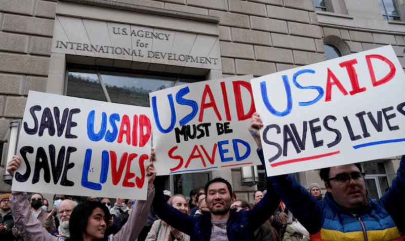 Blow to Trump as Supreme Court blocks bid to withhold payment to foreign aid groups - People hold placards, as the USAID building sits closed to employees after a memo was issued advising agency personnel to work remotely, in Washington, D.C., U.S., February 3, 2025. REUTERS